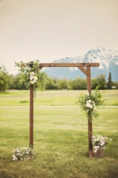 an outdoor ceremony setup with flowers and greenery on the grass in front of mountains