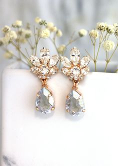 two pairs of earrings on top of a white vase with flowers in the back ground