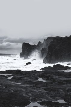 a black and white photo of waves crashing on the rocks in front of an ocean