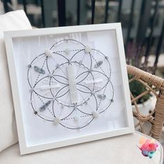 a white framed artwork with beads in the shape of a cross on it sitting on a chair