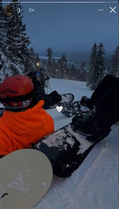 two snowboarders are sitting in the snow with their boards on their feet and one is wearing an orange jacket