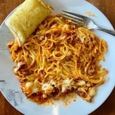 a white plate topped with spaghetti next to a piece of bread on top of a wooden table