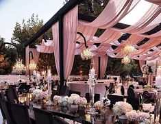 an outdoor wedding reception set up with pink drapes and chandeliers