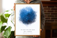 a woman holding up a framed poster with the stars in the night sky on it