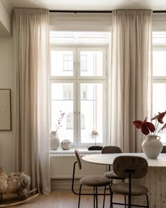 a table and chairs in front of a window with drapes on the windowsill