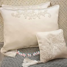 two white pillows with tassels on top of them sitting on a couch next to each other