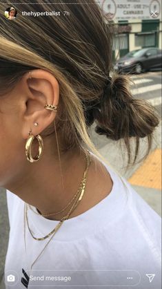 a woman wearing gold earrings and a white t - shirt is looking at her cell phone