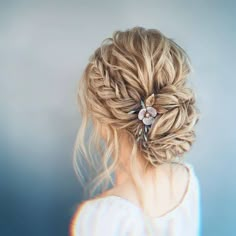 a woman with blonde hair wearing a flower in her hair and braided into a low bun