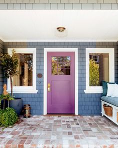 a purple front door on a blue house with white trim and brick walkway leading up to it