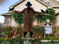 a scarecrow standing in front of a house with crows on his arms and legs