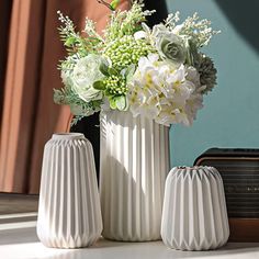 three white vases with flowers in them sitting on a table next to an old radio