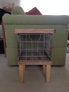 a dog crate sitting on top of a wooden table in front of a couch with a green cover