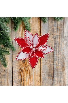 a red and white poinsettia on top of a wooden table next to pine branches