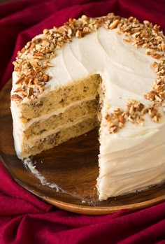 a cake with white frosting and pecans on top sitting on a wooden plate