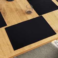 three black mats on top of a wooden table next to a drink glass and cup