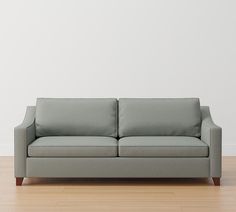 a gray couch sitting on top of a hard wood floor next to a white wall