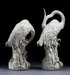 two white sculptures with birds on them sitting in front of a black background and one is holding its head