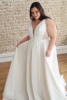 a woman in a white dress standing on a hard wood floor next to a brick wall