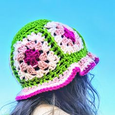 a woman wearing a crocheted hat with flowers on the front and side, against a blue sky