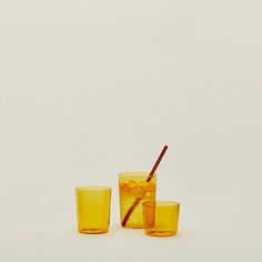 three glasses filled with orange liquid and one has a straw sticking out of the top