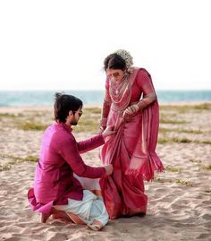 a man kneeling down next to a woman in a pink sari on the beach