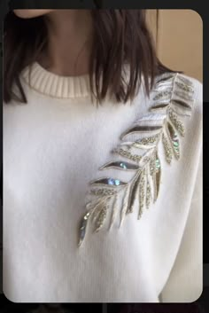 a woman wearing a white sweater with gold leaf brooch on the front and back