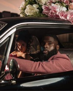 a man sitting in the drivers seat of a car with flowers on top of his head