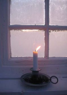 a lit candle sitting on top of a window sill in front of a window