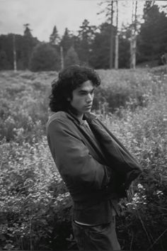 a black and white photo of a man standing in a field with wildflowers