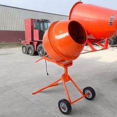 an orange cement mixer sitting on wheels in front of a building