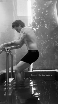 a man with tattoos standing in a pool next to a metal hand rail and looking down at the water