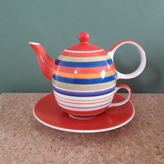 a colorful tea pot and saucer sitting on top of a red saucer plate