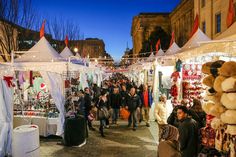 many people are walking through an outdoor market with christmas decorations and lights on the buildings