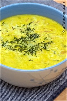 a blue bowl filled with yellow soup on top of a cloth covered place mat next to a wooden table