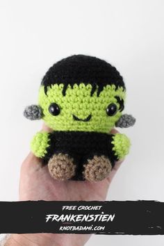 a hand holding a small crocheted green and black creature