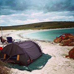 a tent pitched up on the beach next to some water and people standing around it