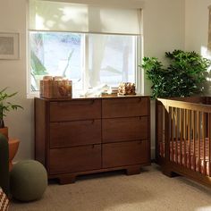 a baby's room with a crib, dresser and potted plants in it