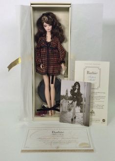 a barbie doll in a box with an old photo and card on the table next to it