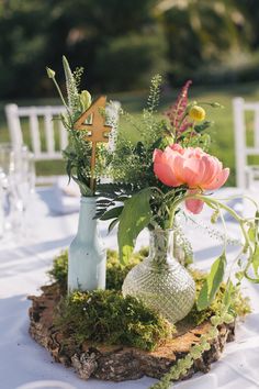 three vases with flowers and greenery are on a wooden slice at the table