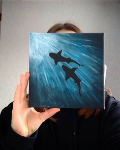 a woman holding up a painting with two sharks on it