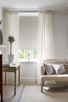 a living room filled with furniture and a window covered in white draping next to a table