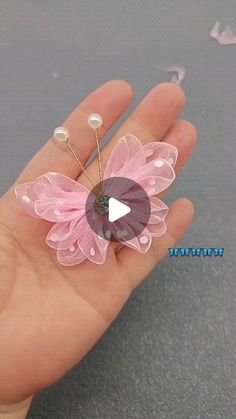 a hand holding a tiny pink flower brooch on it's finger with pearls