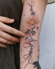 a woman's arm with flowers and birds tattoo on her left arm, which is holding a cat