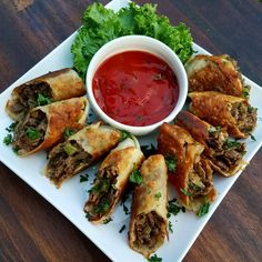 a white plate topped with pastries covered in meat and veggies next to a bowl of ketchup