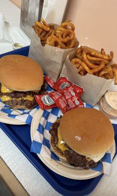 two cheeseburgers and some onion rings on a blue tray with white checkered napkins