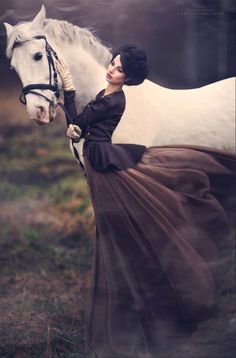 a woman in a dress standing next to a white horse