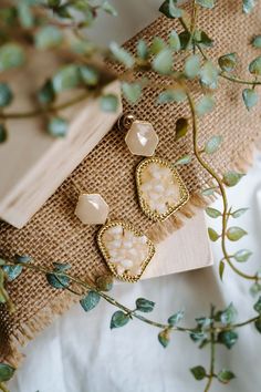 the earrings are sitting on top of a piece of wood next to some plants and leaves