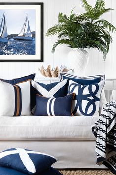 a white couch with blue and white pillows on it next to a potted plant