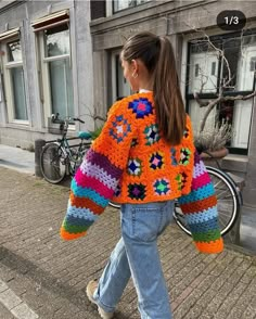 a woman is walking down the street wearing an orange crocheted sweater and jeans