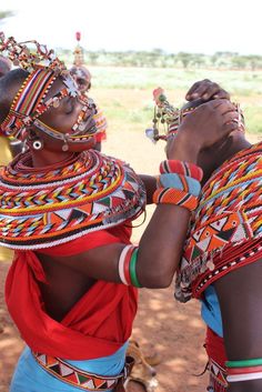 two women dressed in colorful clothing standing next to each other with their hands together and looking into the distance